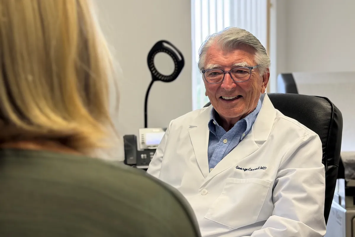 Dr. Carroll smiling as he talks with a woman seated across his desk, her back to the camera